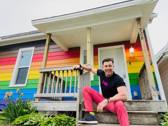 Robert Geller sits on the front porch of a rainbow-painted home